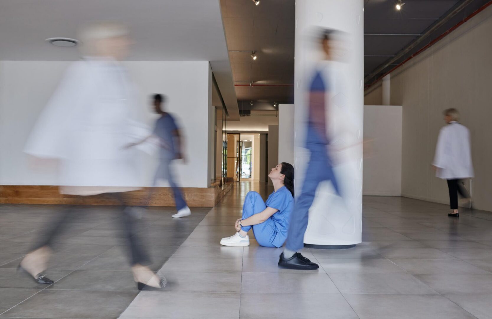 Shot of a young female doctor looking tired while working in a busy hospital Nurse in scrubs sitting on hospital floor